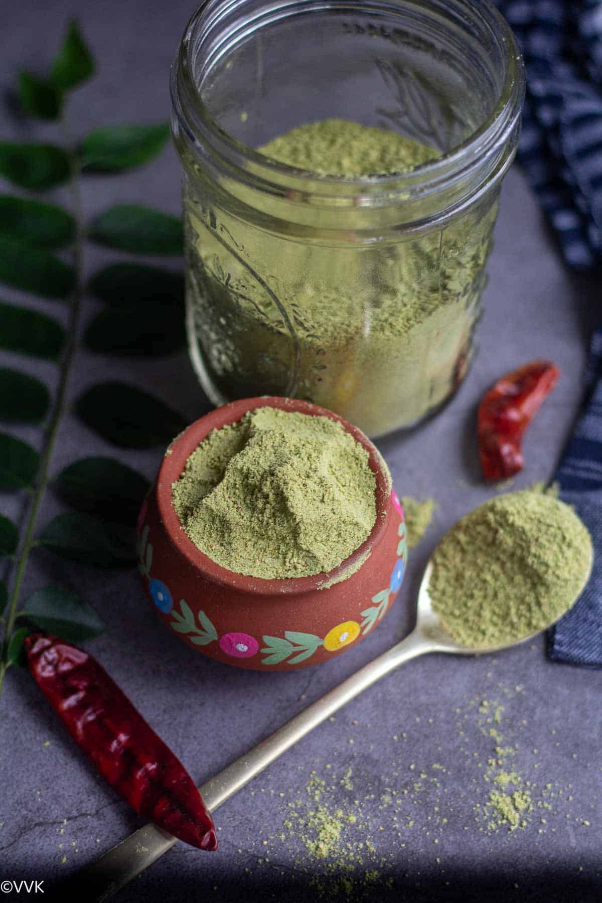 karivepaku podi in clay pot with curry leaves and red chilies on the side