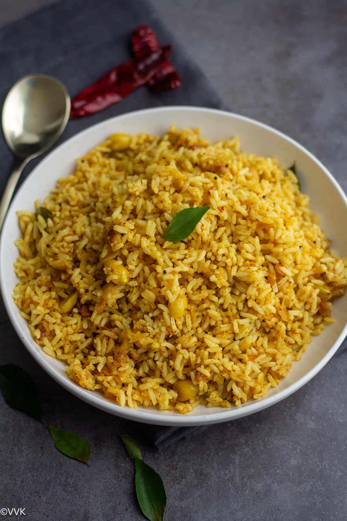 mamidikaya pulihora in a white plate with a single curry leaf on top