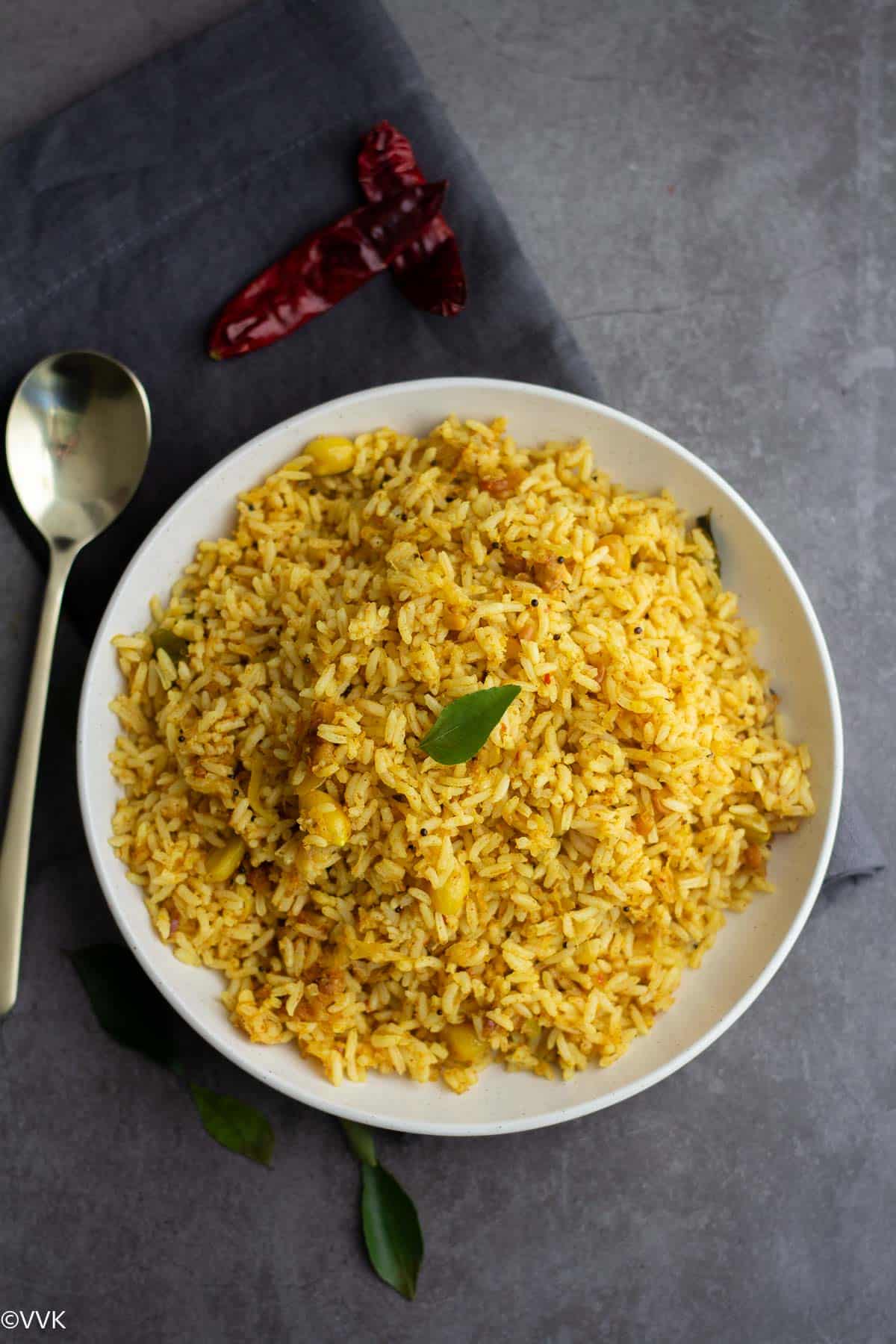 overhead shot of raw mango rice with curry leaf on top and with a spoon on the side.