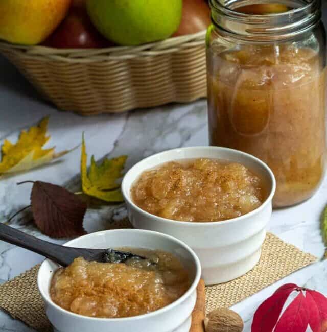 homemade applesauce served in two white bowls and also in glass jar with apples on the side