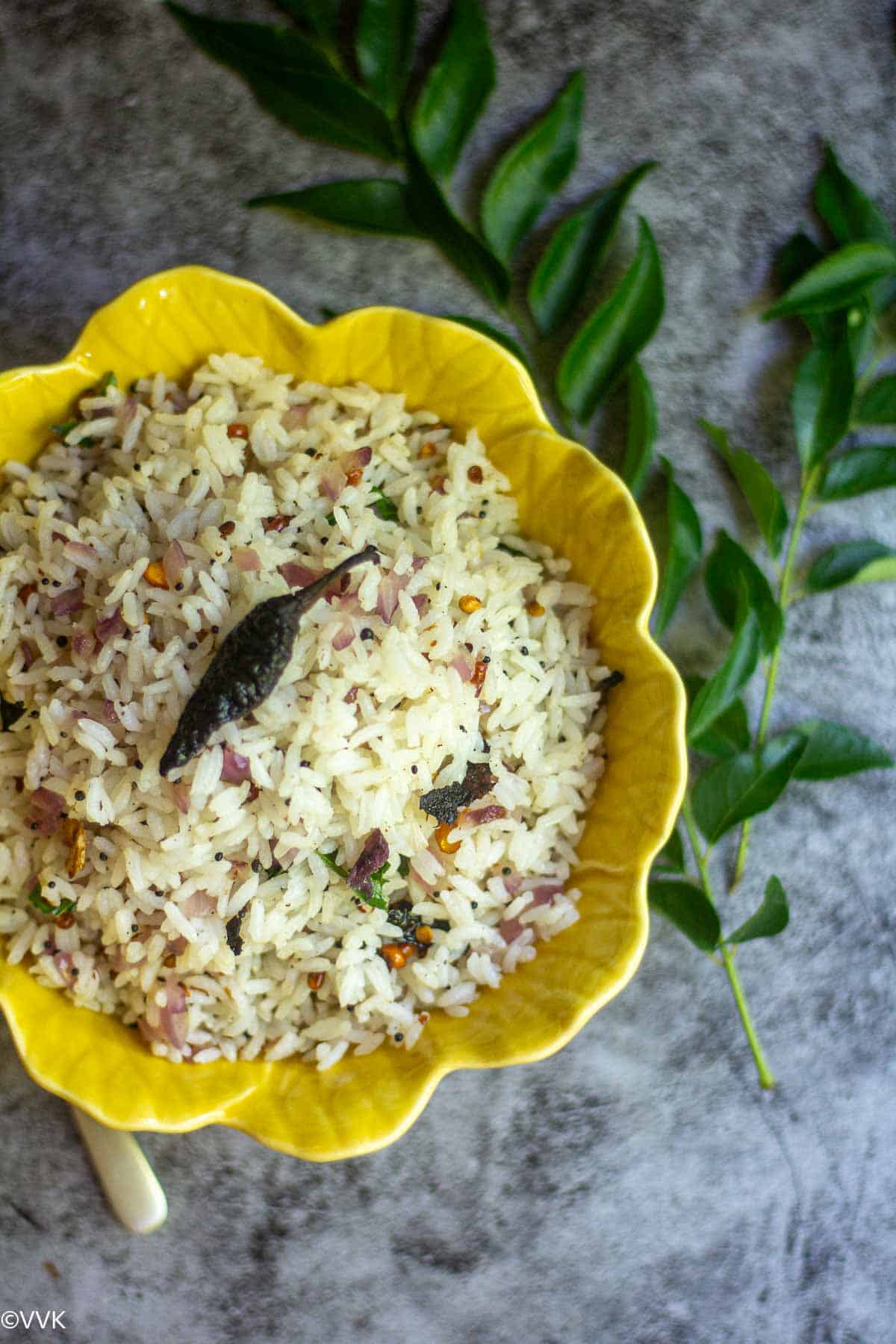 overhead shot of thallipu sadam served in yellow bowl with curry leaves on the side