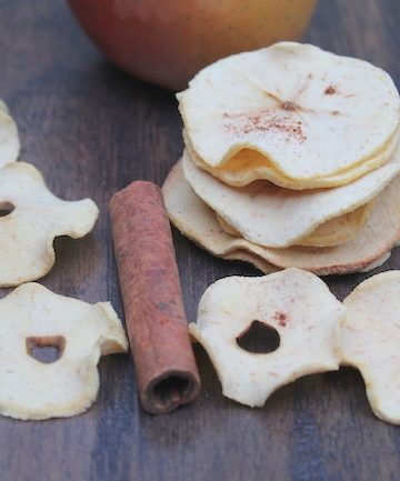 A stack of Baked Apple Chips on a table with an apple and a cinnamon stick among the chips