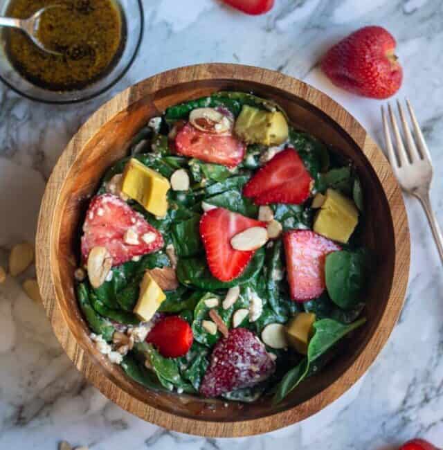 overhead shot of spinach and strawberry salad in a wooden bowl with the dressing on the side