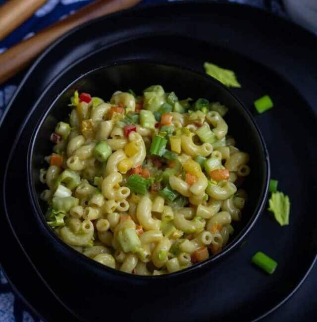 classic pasta salad in a black bowl with some celery greens on the side.