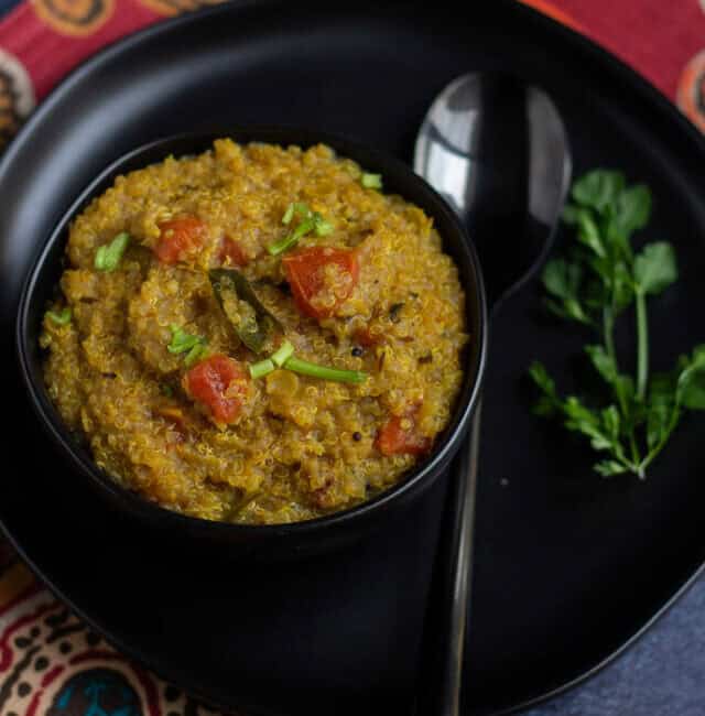 quinoa rasam rice on a black bowl placed on a black plate on a red fabric