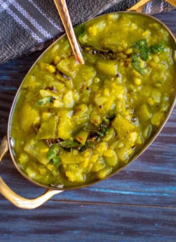 top angle shot of ridge gourd curry in a brass serve ware with a spoon inside