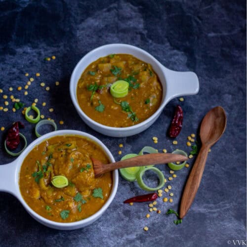 square image of leeks sambar in white bowls with wooden spoon on the side