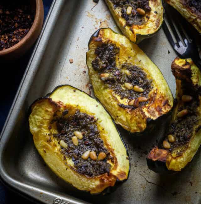 close up shot roasted acorn squash with pesto and pine nuts