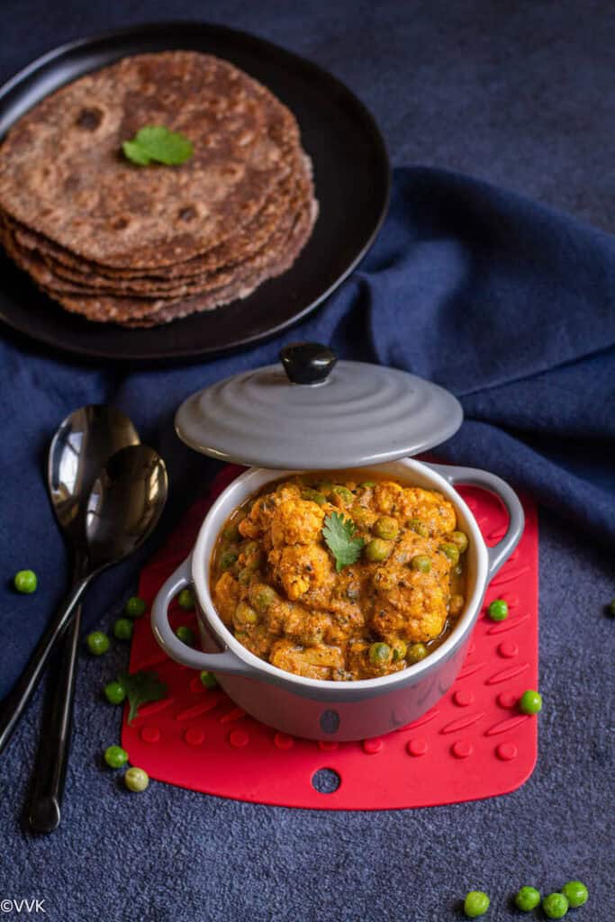 gobi matar served in a gray casserole placed on a red coaster with ragi rotis on the top