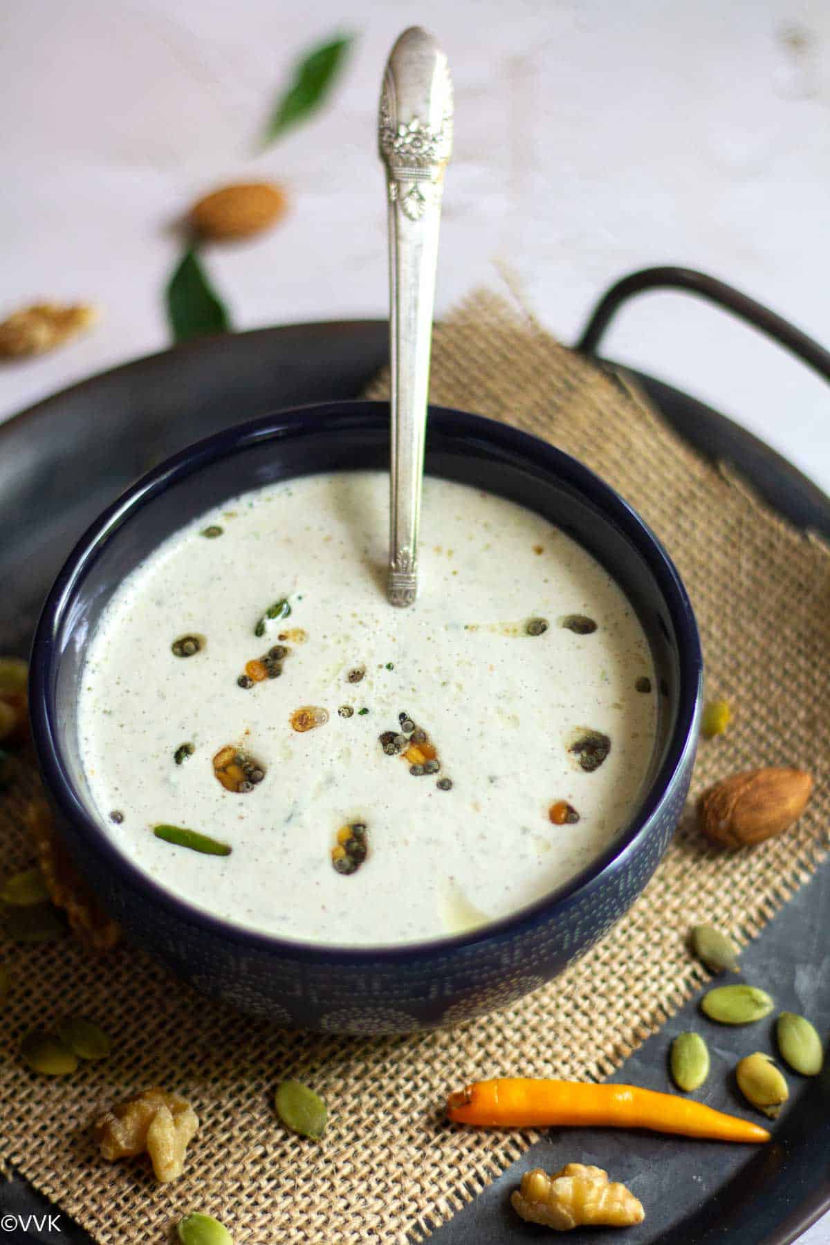 coconut chutney with nuts served in a bowl with a spoon inside placed on a burlap cloth with nuts on the side