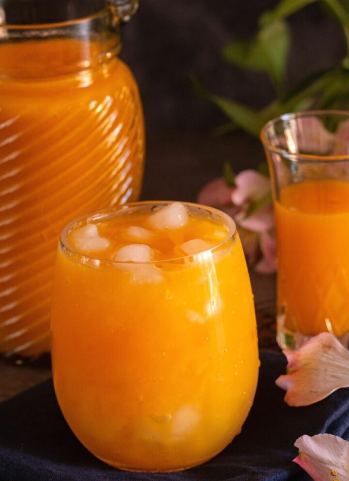 square image of mango juice served in tall glass with the concentrate behind