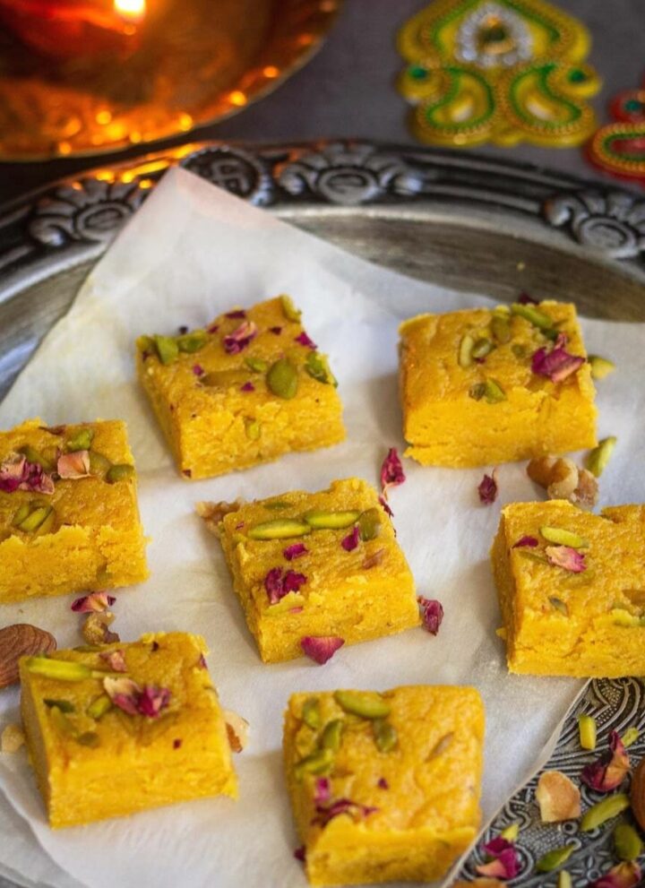 square image of milk barfi placed on silver tray with parchment paper