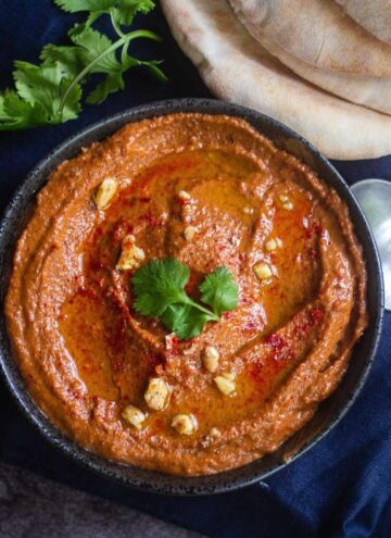 close up shot of muhammara served in bowl with pita bread on the side placed on a blue towel