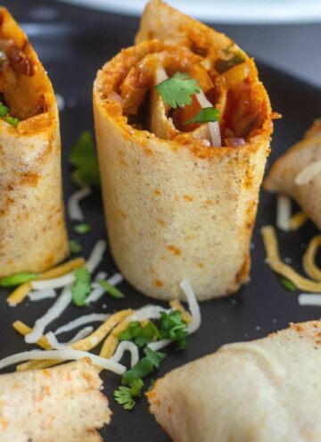 single jini dosa roll served in black plate with cheese drizzled