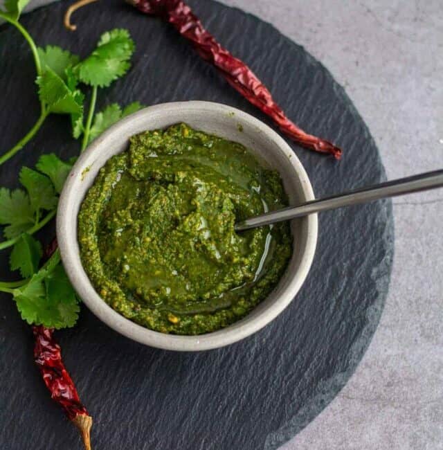 kothamalli chutney served in white ceramic bowl placed on black slate board with chilies and cilantro on the side