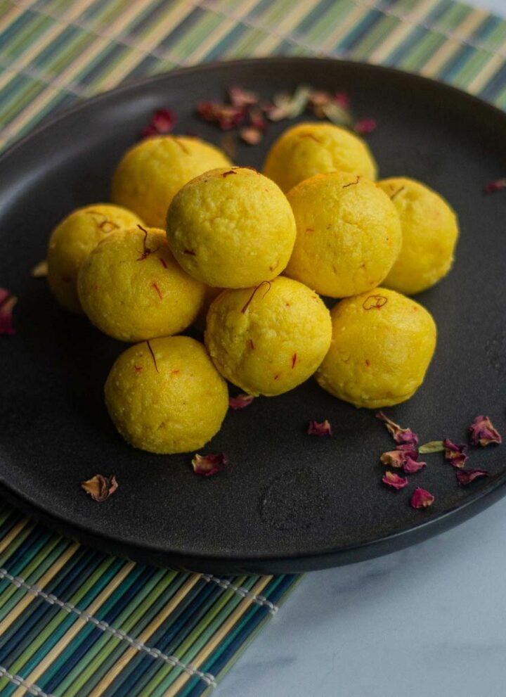 paneer ladoo stacked on black plate placed on a green mat with rose petals on the side