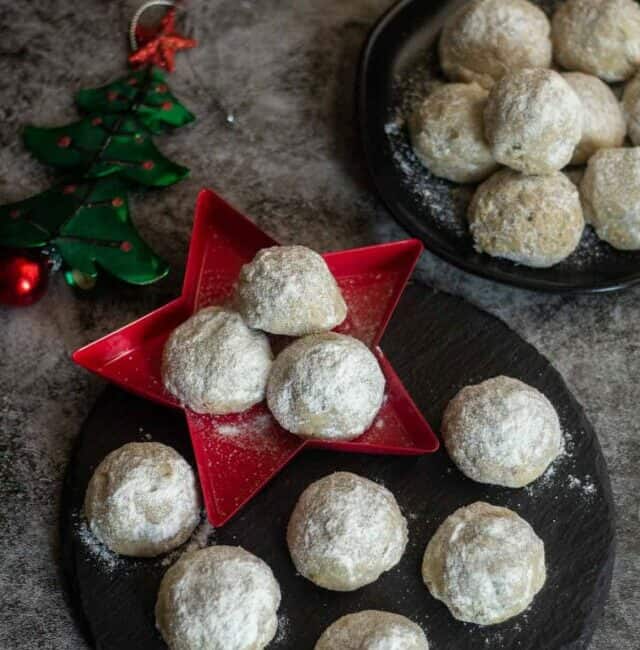 snowball cookies placed on blackplate and star plate with xmas tree on a side