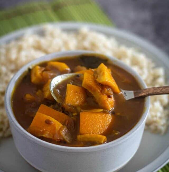 close up shot of orange peel kuzhambu with spoon inside served with rice