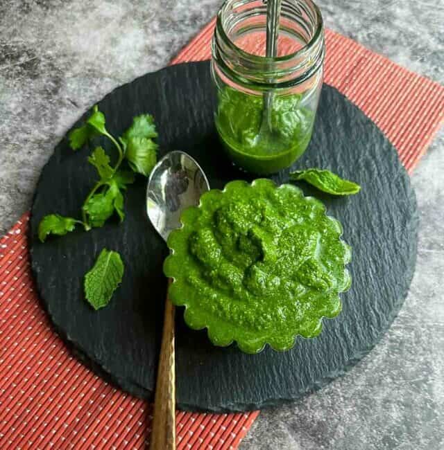 mint and cilantro chutney in a bowl and jar placed on black board on top a red mat