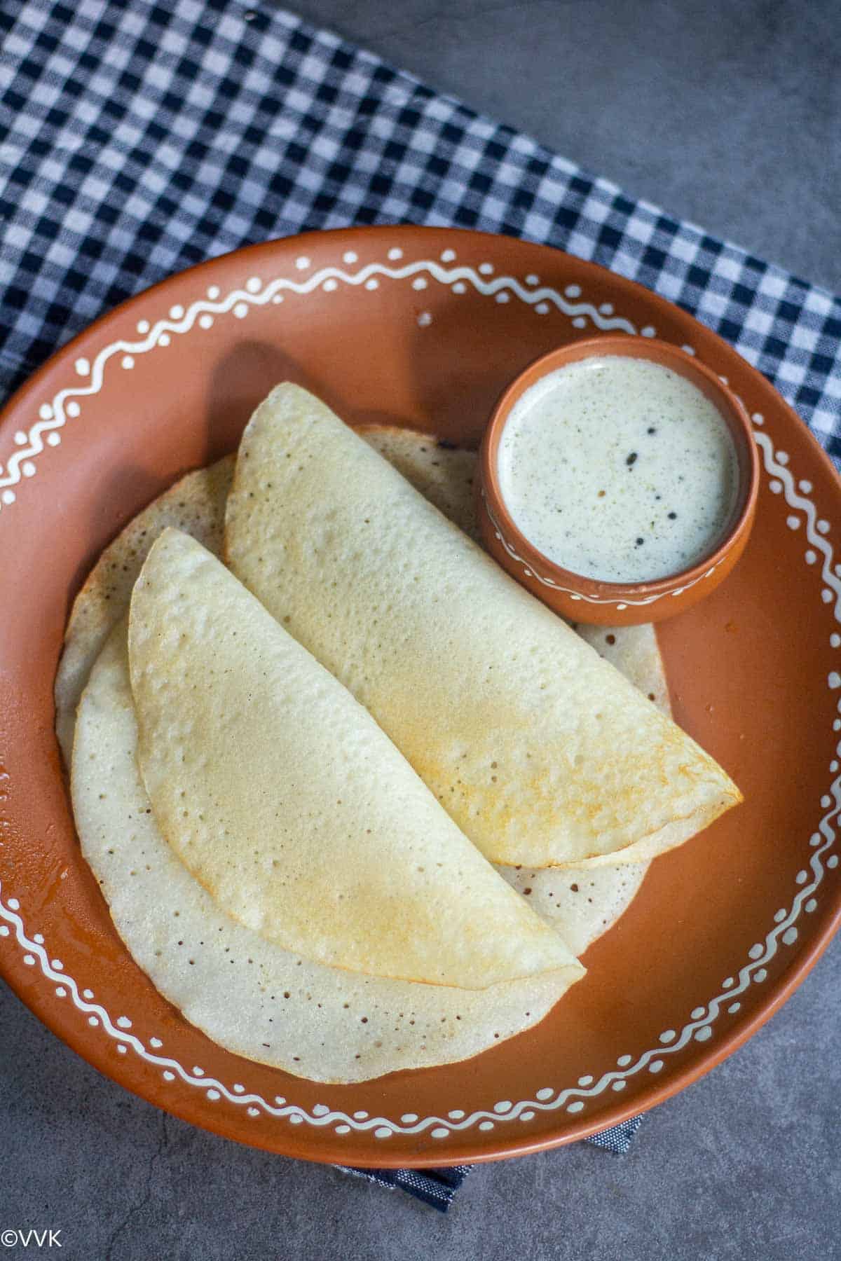 overhead shot of watermelon rind dosa folded on a mud plate with chutney