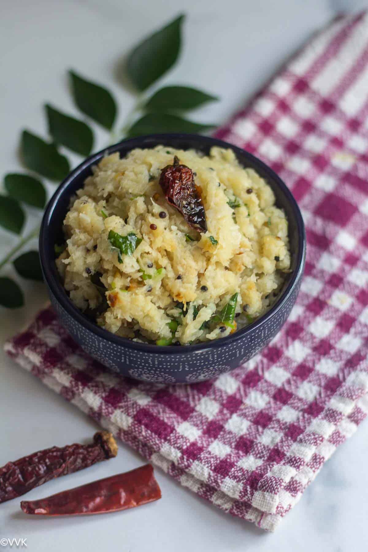 close up shot of mullangi thuvattal served in blue bowl with curry leaves on the side