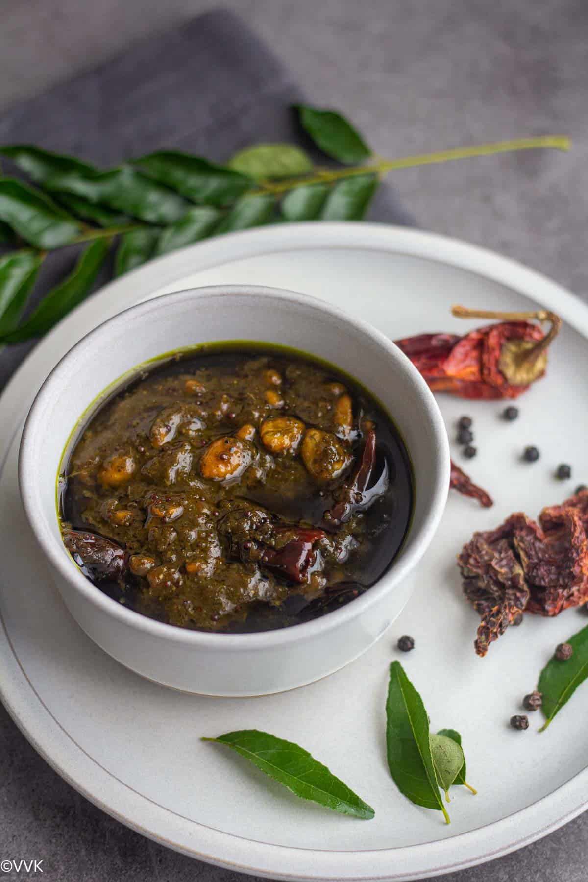 curry leaves pulihora served in a bowl with pepper corns, curry leaves and red chilies on the side