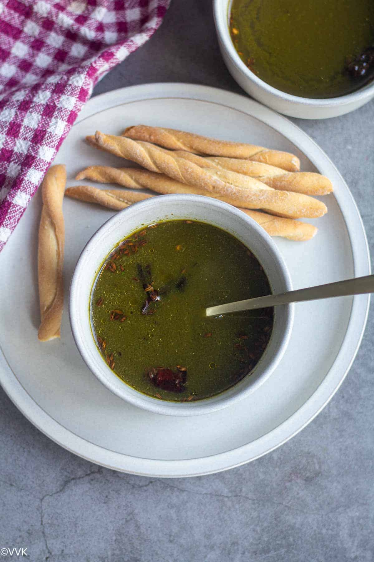 overhead shot of moringa leaves soup with bread sticks