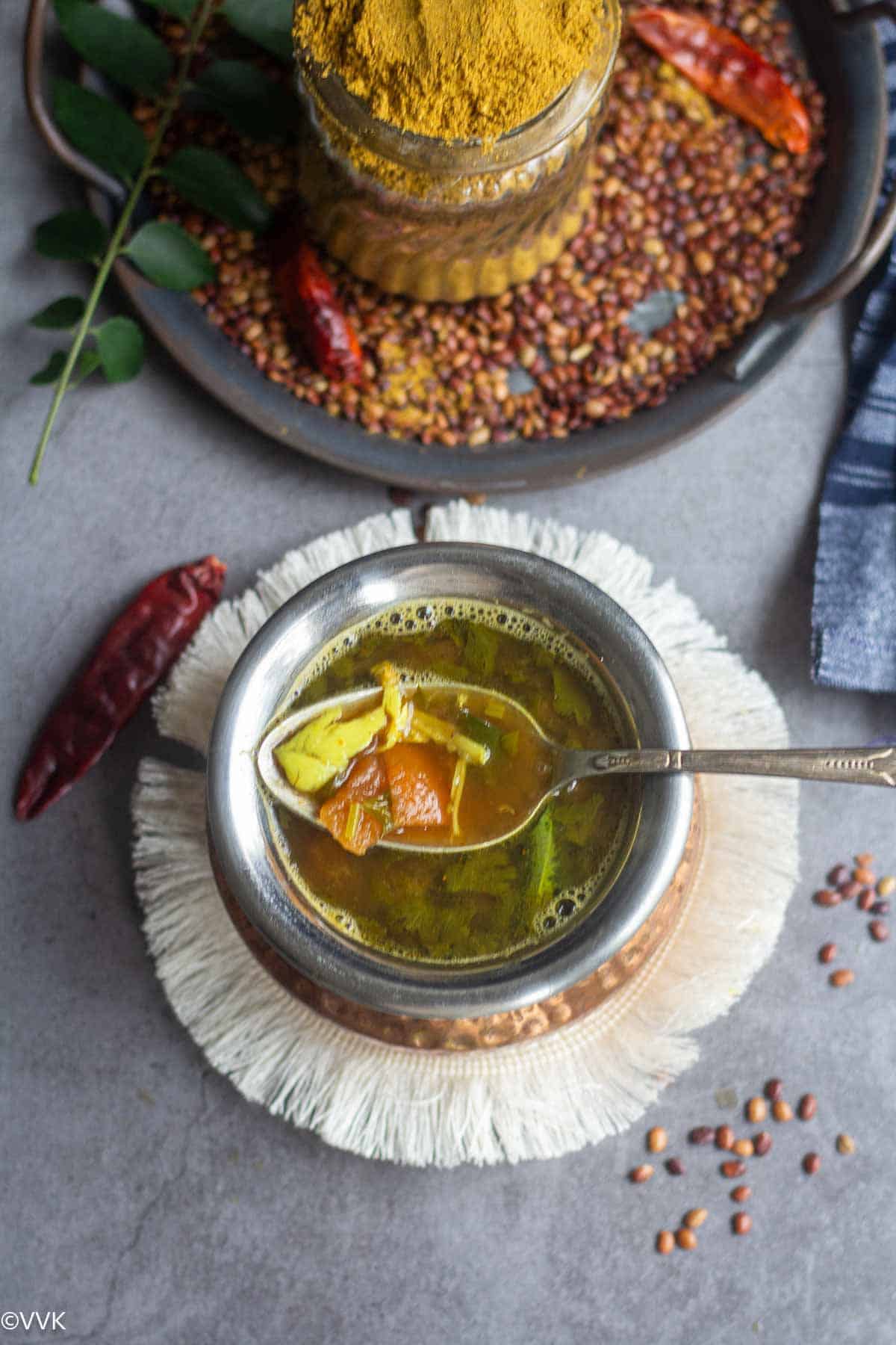 overhead shot of horsegram rasam with spoon inside