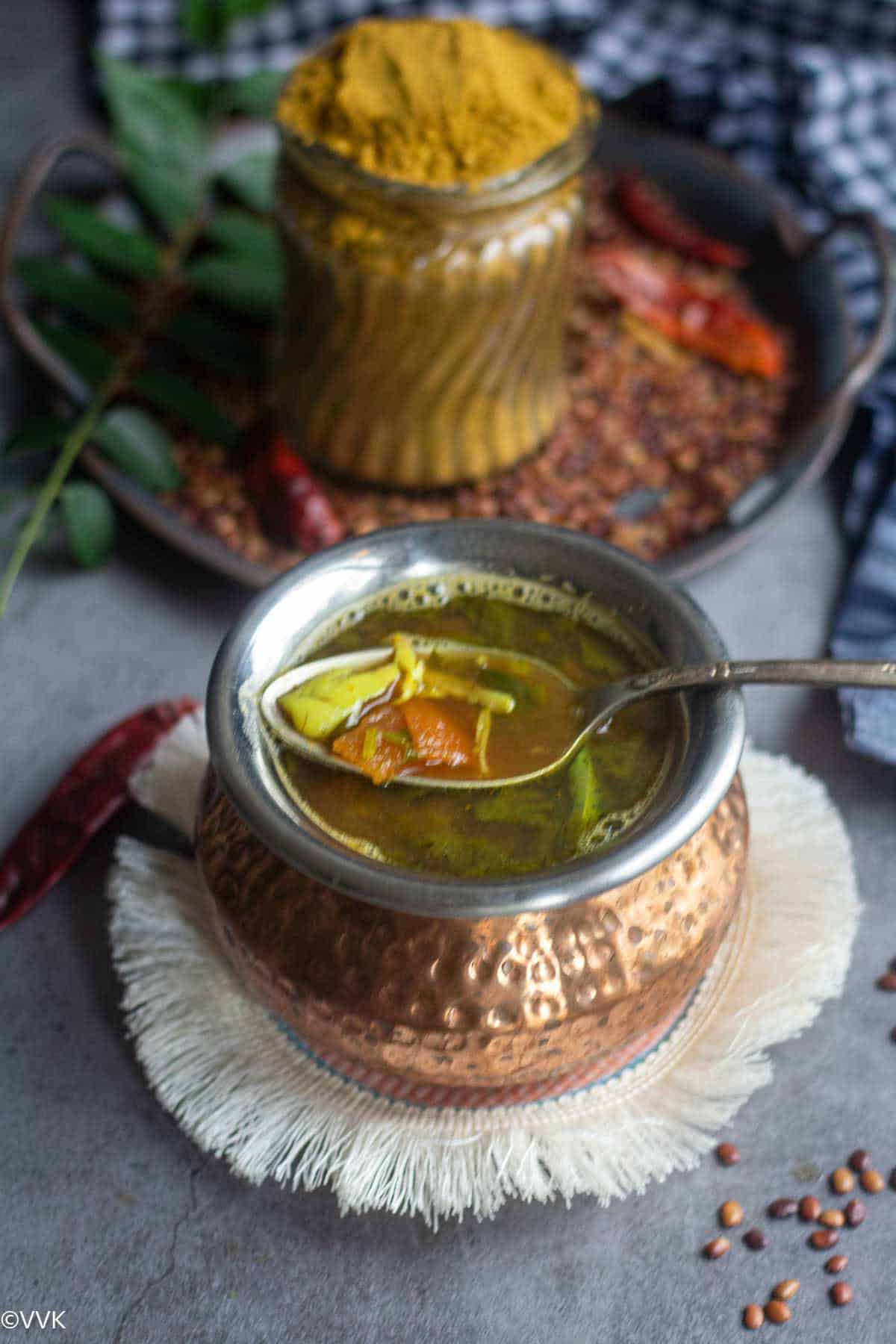 slanting shot of rasam in a bowl with spoon inside