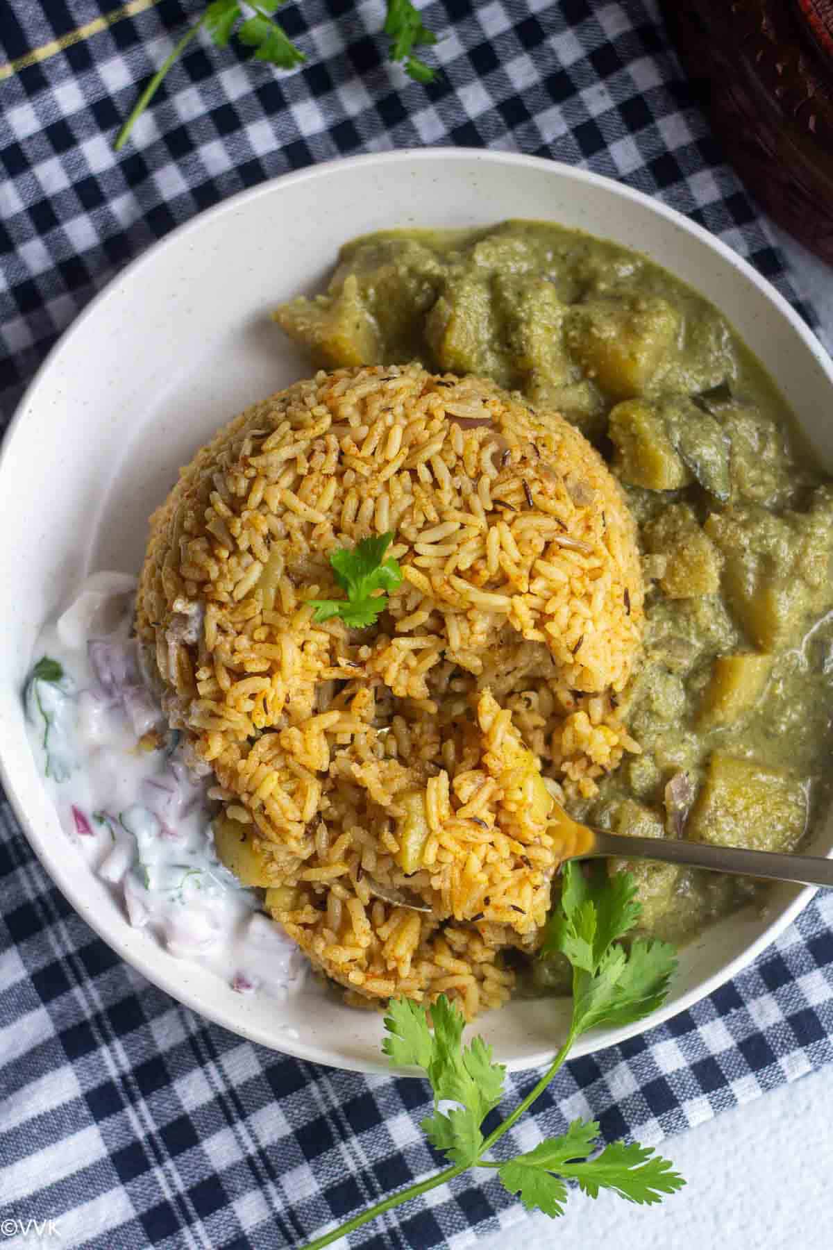 zucchini rice with spoon inside with kurma and raita. An action of rice mixed