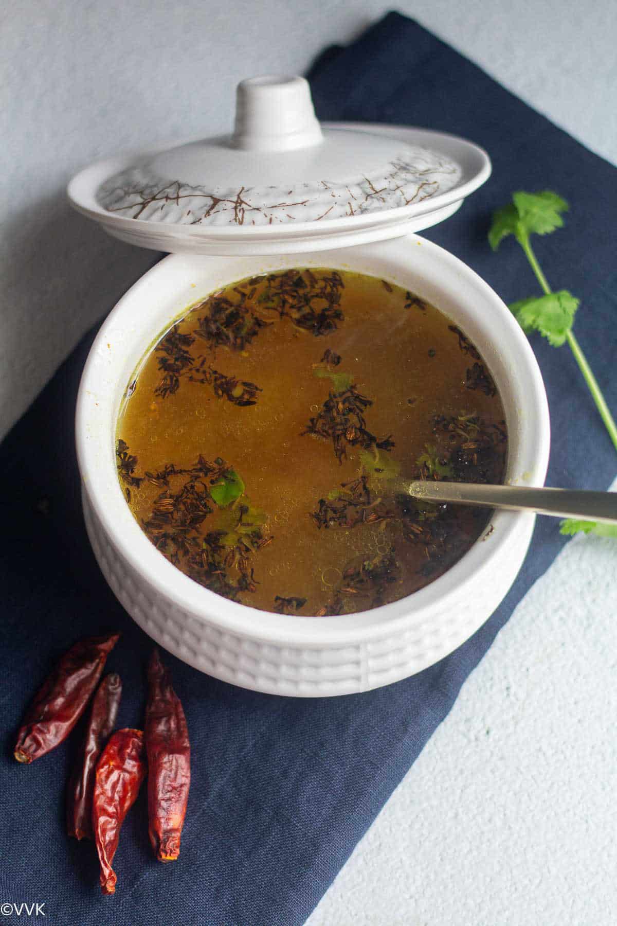 close up shot of dried neem flower rasam with a spoon inside