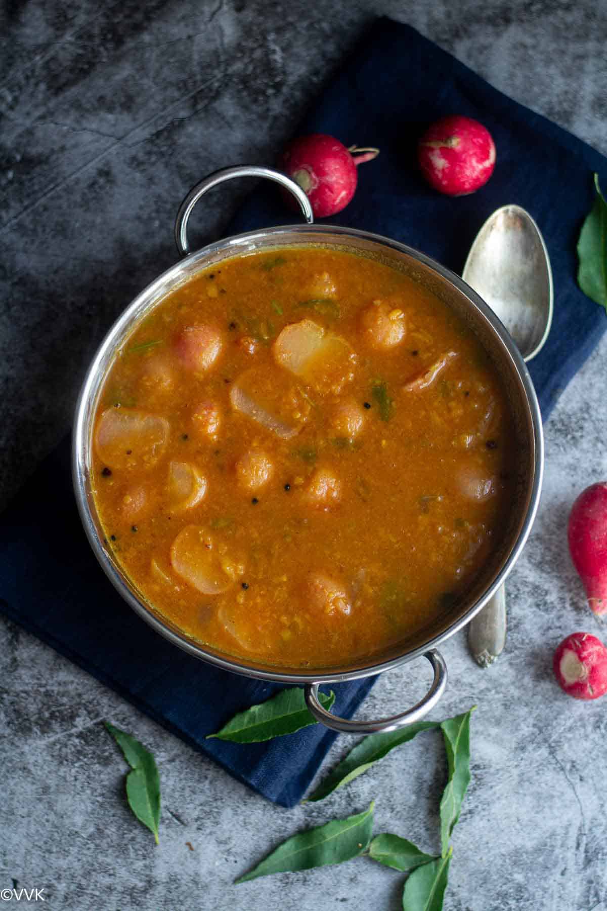 overhead shot of red radish sambar with some red radish and curry leaves on the side