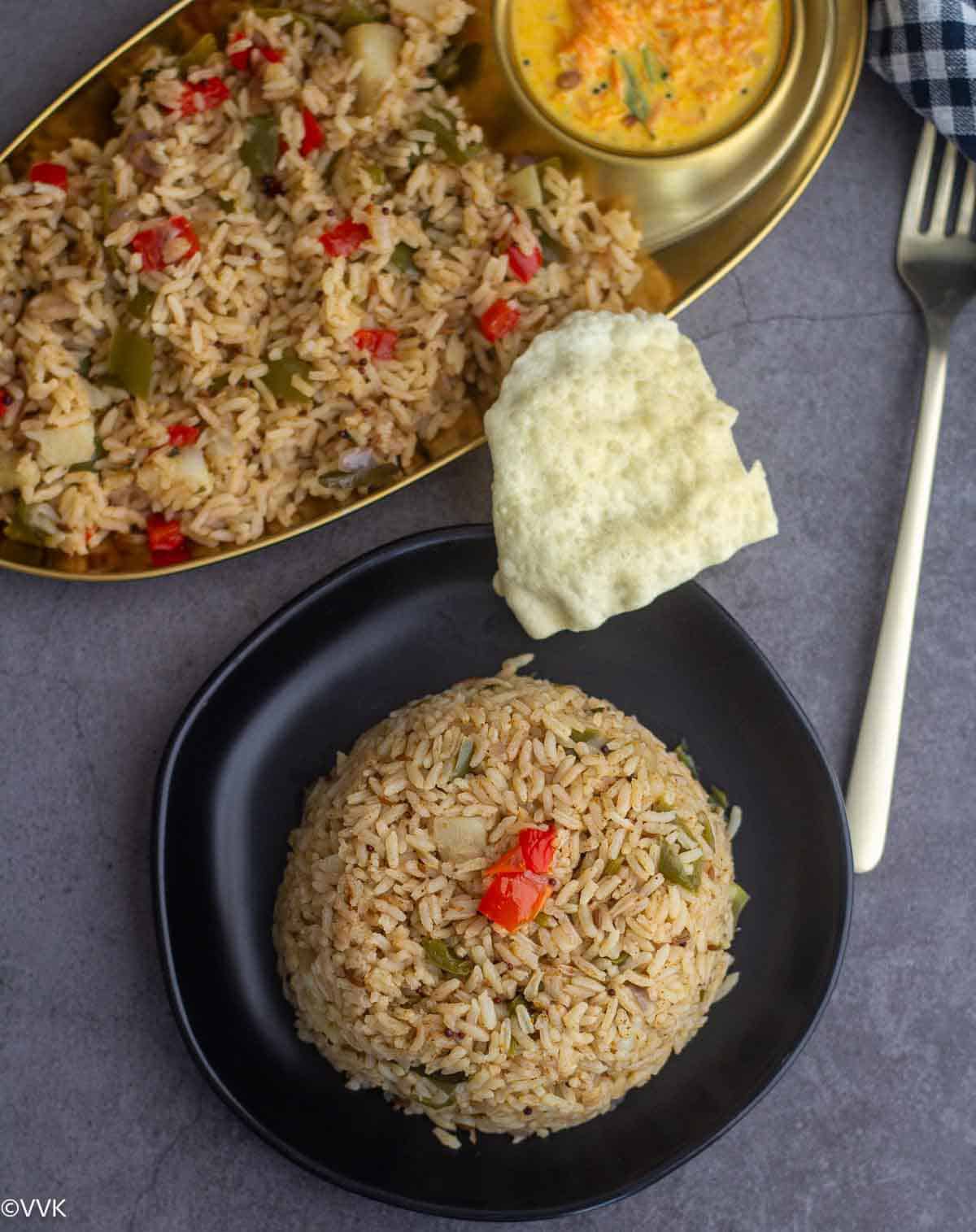 potato capsicum rice with papad and raita on black and golden plate