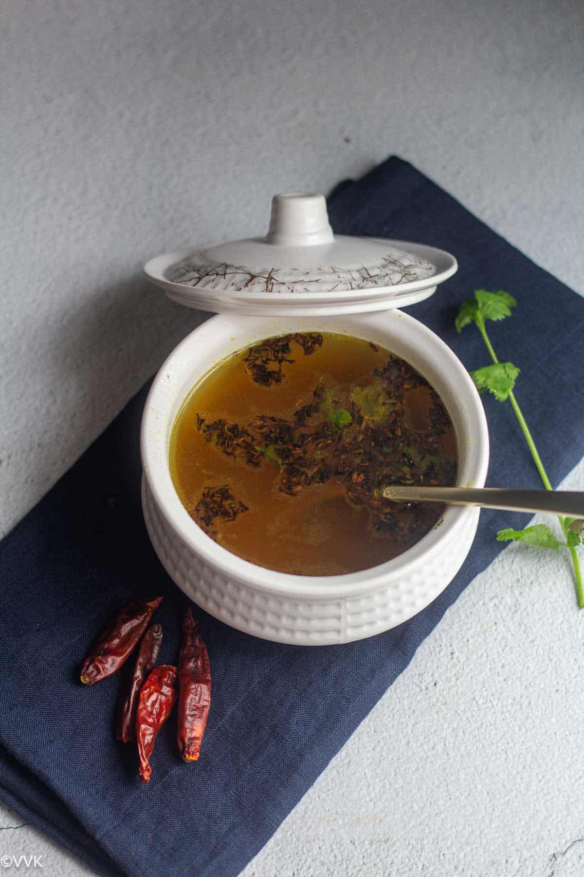 overhead shot of neem flower rasam in whtie bowl with some dried red chilies and cilantro in the side