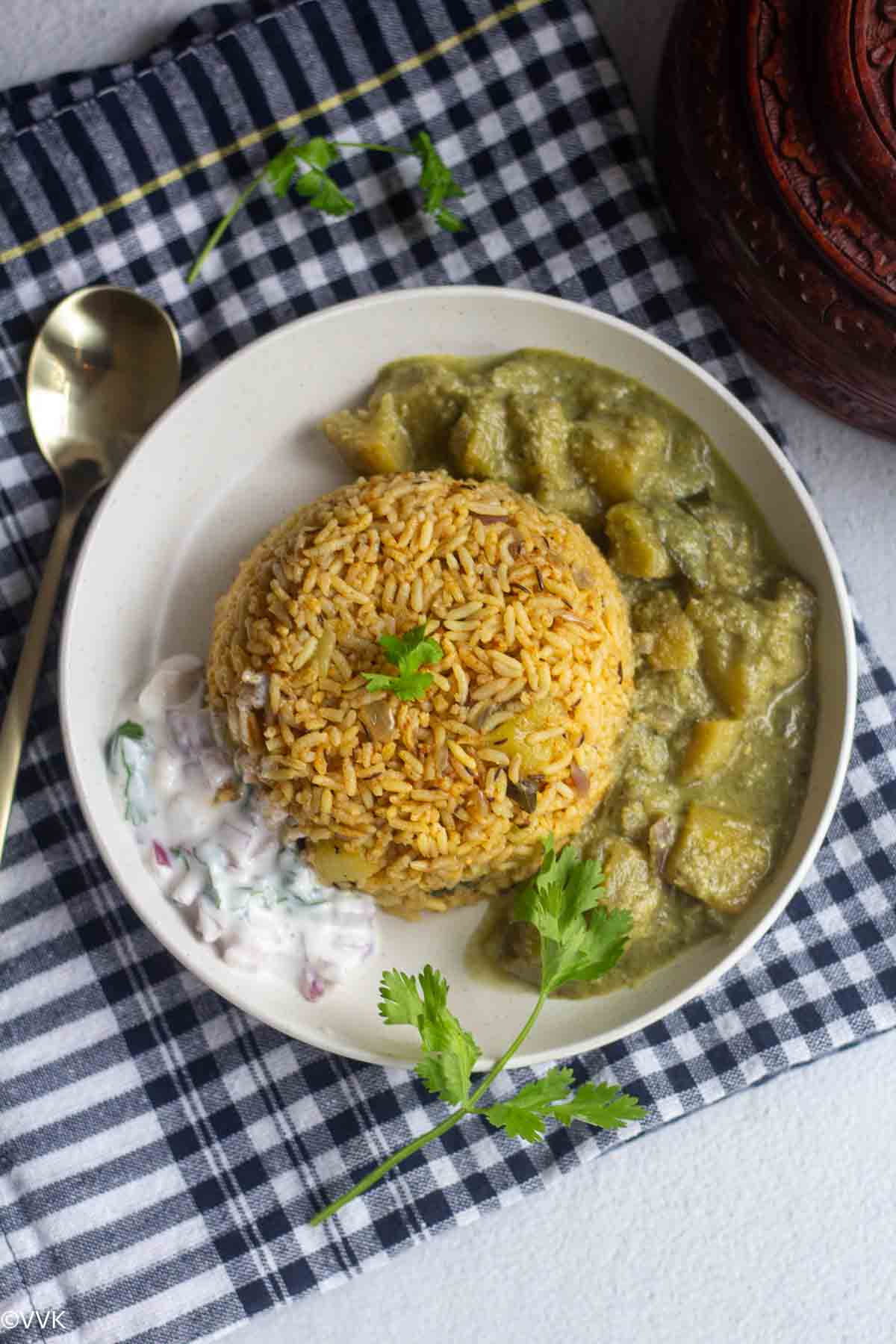 overehead shot of zucchini rice served in white plate with raita and kurma