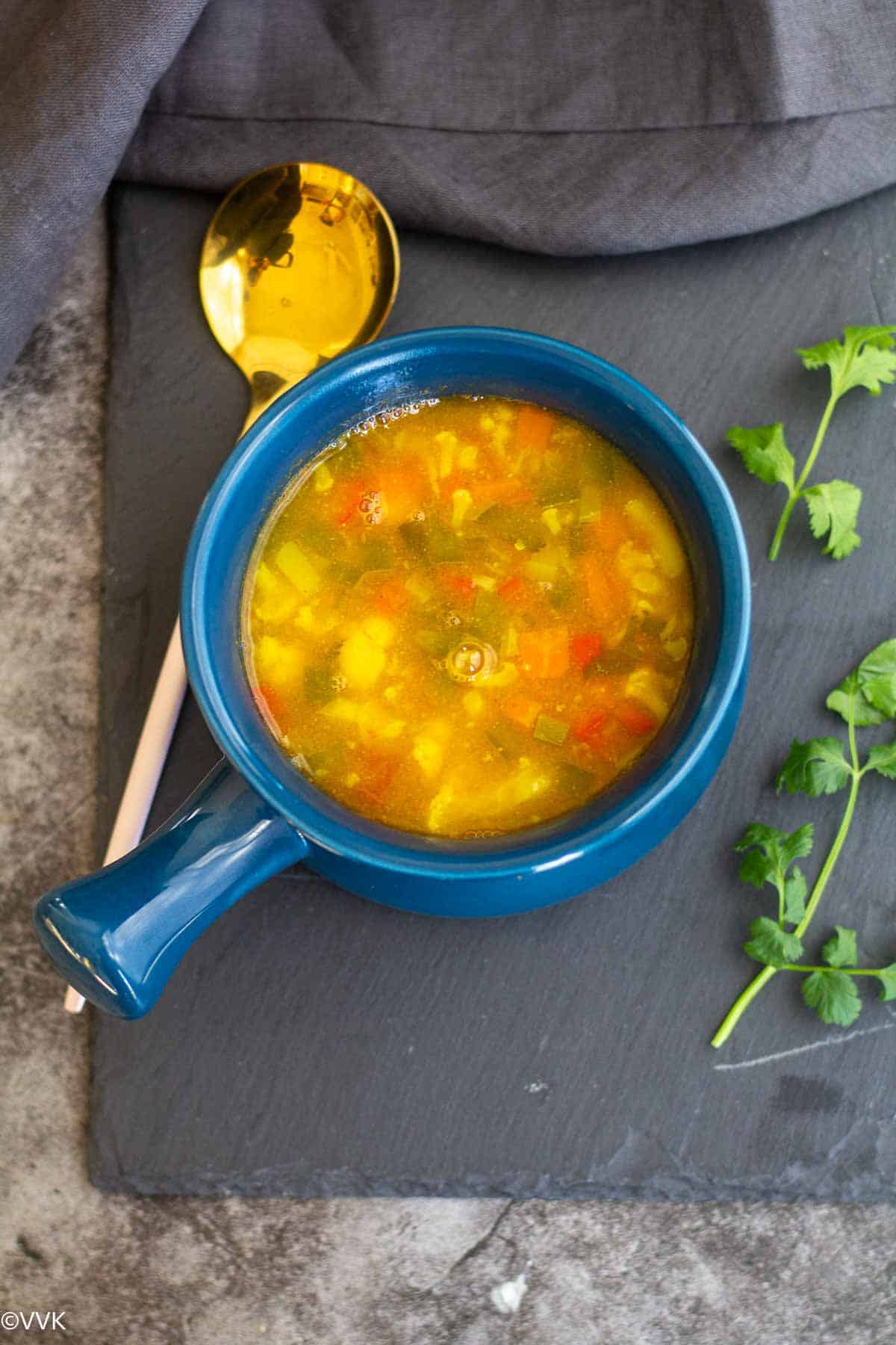 over head shot of barley and vegetable soup with masoor dal served in a blue bowl with spoon on the side