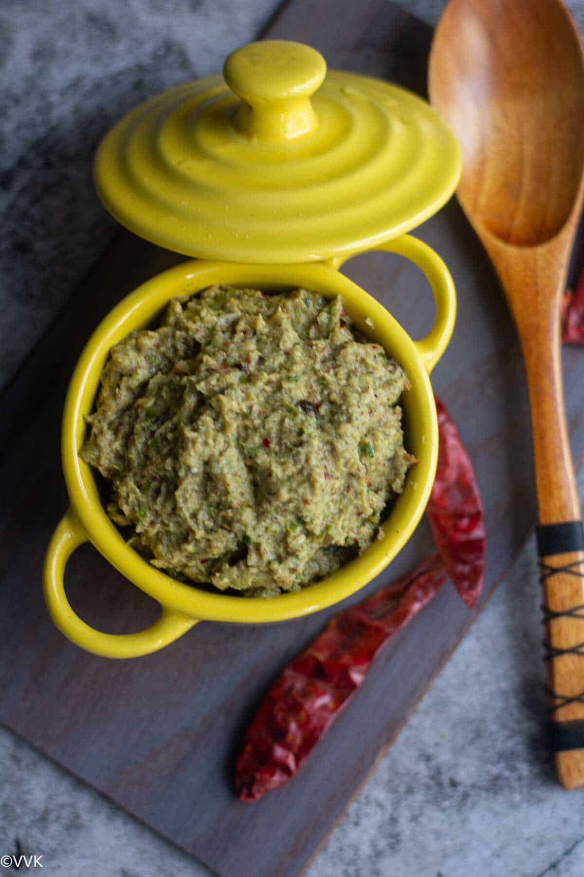 overhead shot of tindora chutney served in yellow casserole with red chilies on the side